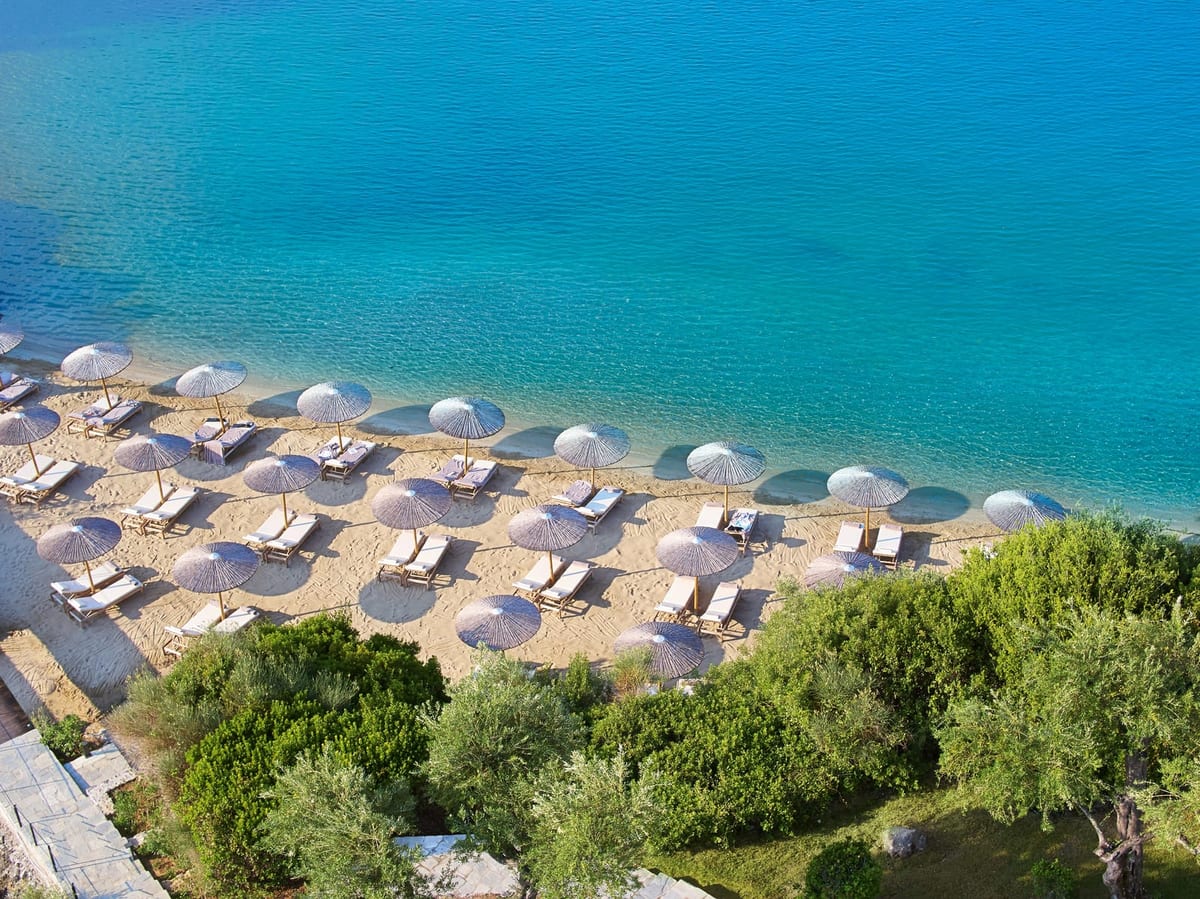 Straw umbrellas and loungers on a sandy cove, Grecotel Corfu Imperial