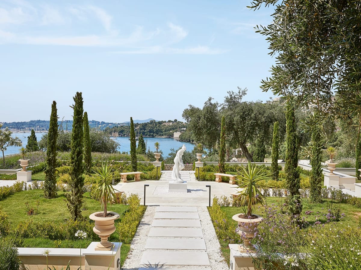 Marble garden walk with cypress and a statue looking over Kommeno bay