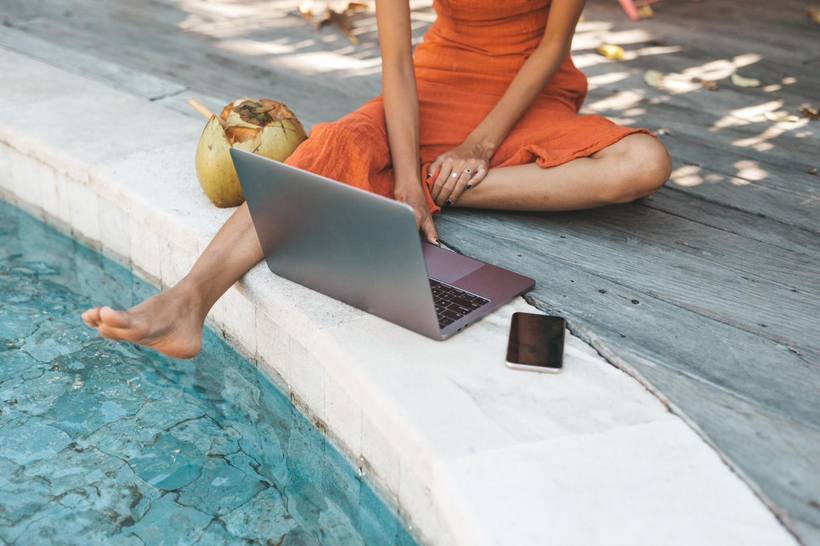 A laptop open at the edge of a pool, feet in the water